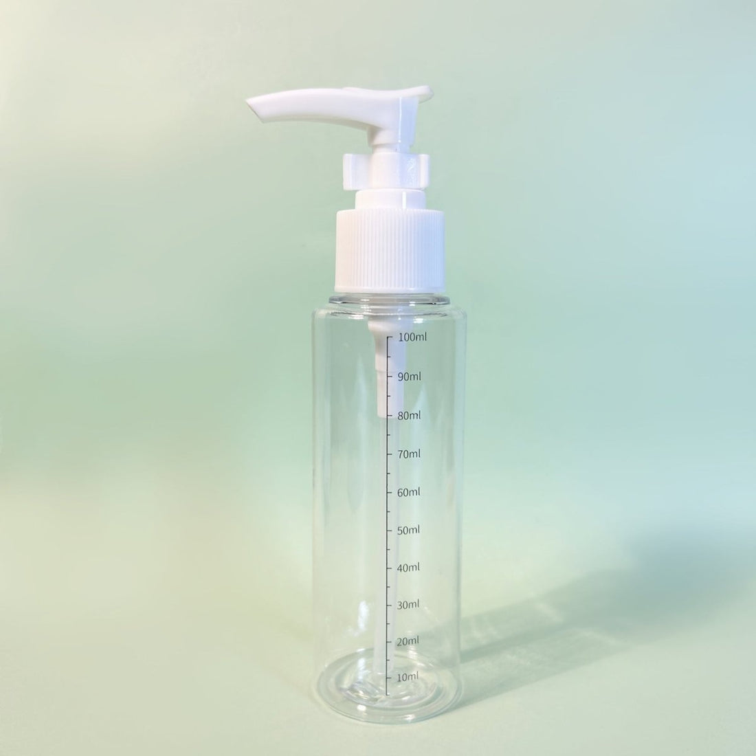 Clear plastic pump bottle, white dispenser head and front measurement scale up to 100ml.