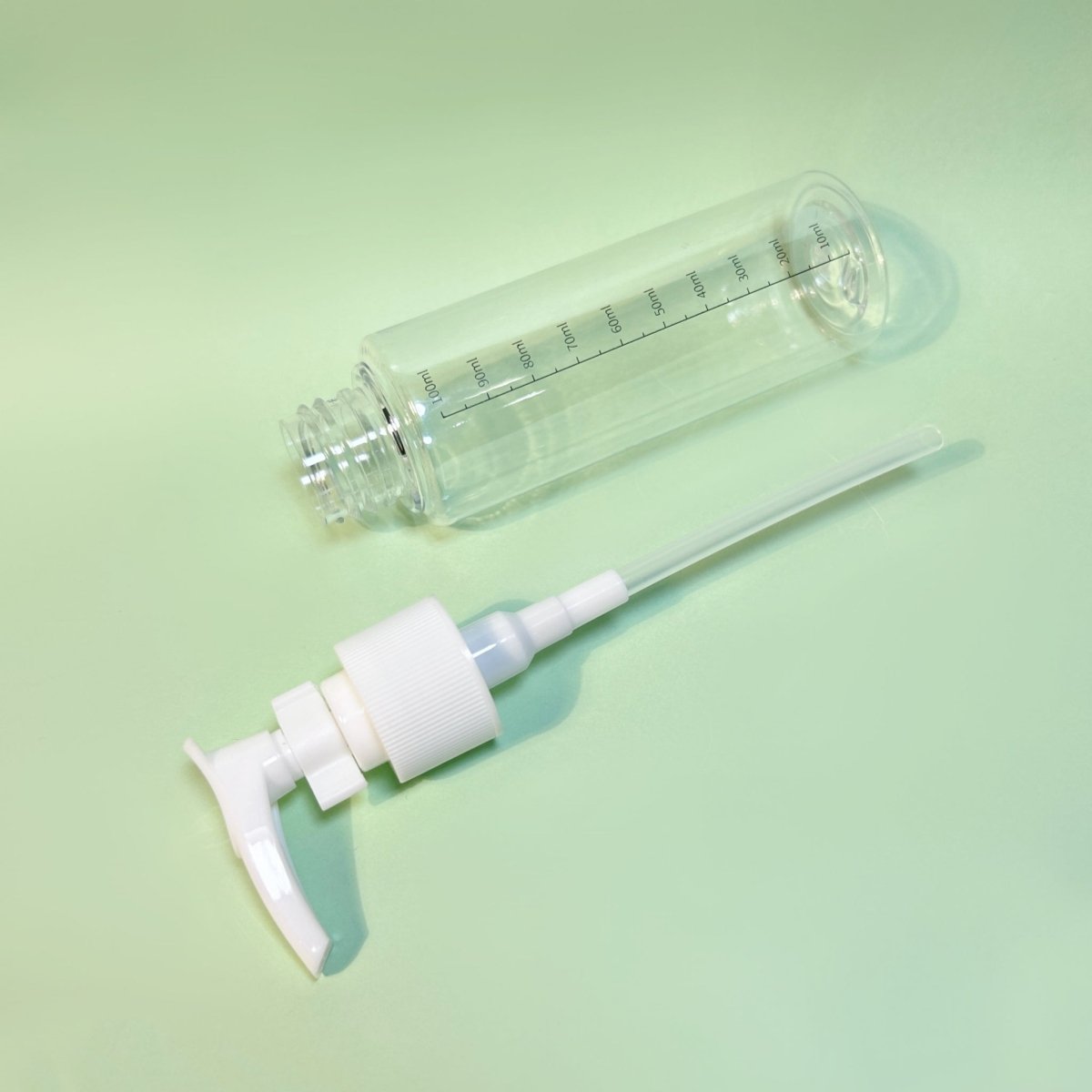 Clear 100ml plastic pump bottle with white sprayer, side view and measurement marks.