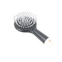 Black round cushion hair brush with white pin bristles and dark handle