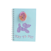 Light blue spiral notebook with pink orb graphic and "TRY TO FLY" text on cover