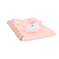Pink spiral notebook with silicone charms on front cover, angled view