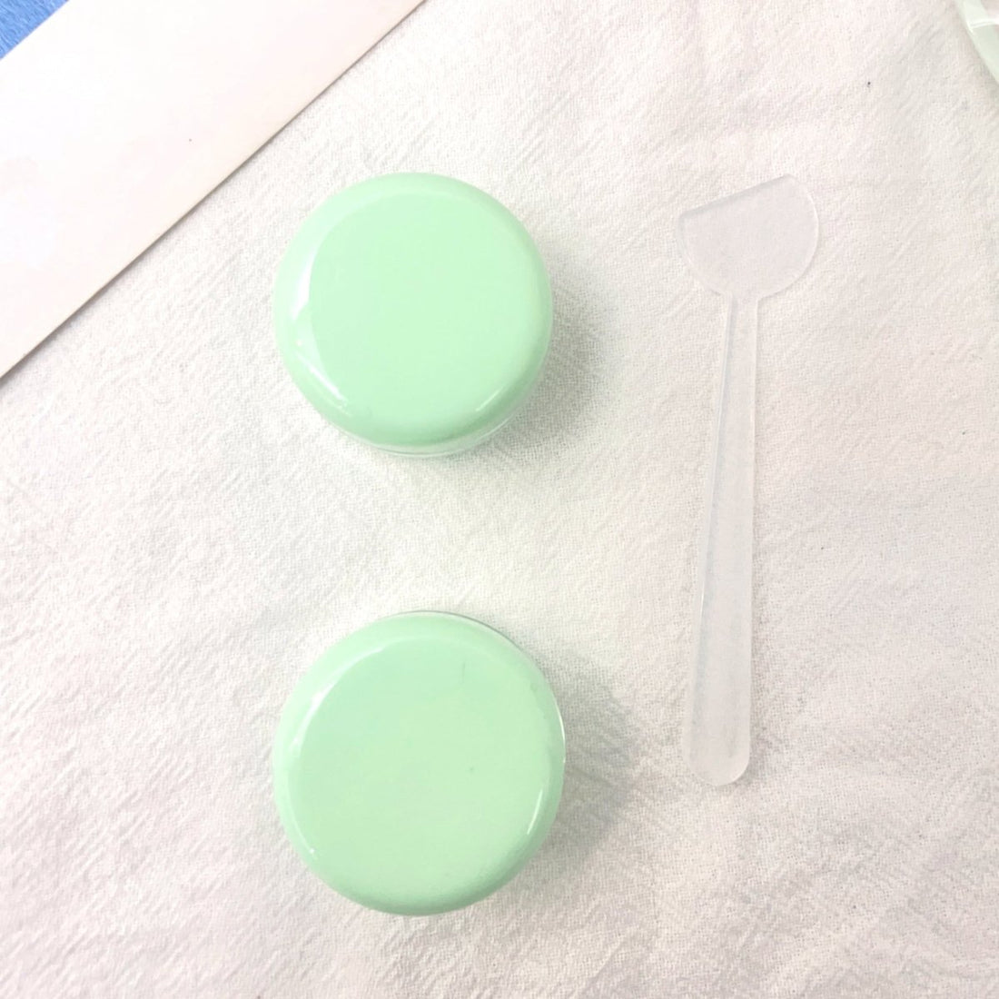 Two mint green cream jars with glossy round lids and clear spatula