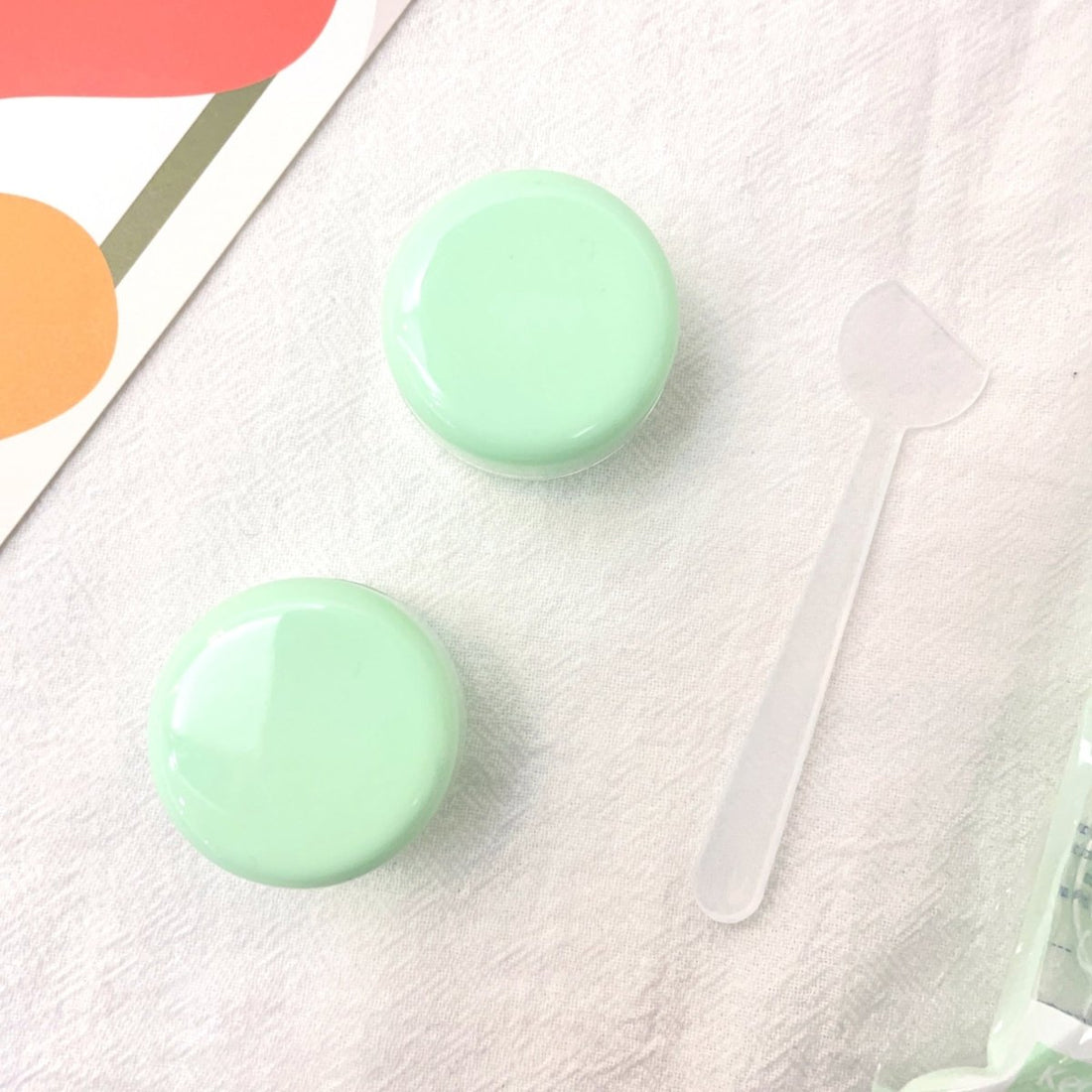 Two mint green cream jars and a clear spatula, round glossy lids