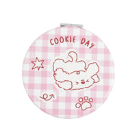 Round compact mirror with pink gingham background and outlined cookie day puppy