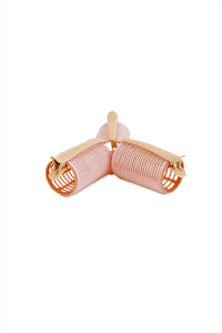 Three light pink hair rollers with beige end clips, angled view