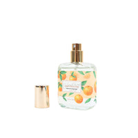 Eau de toilette bottle with gold cap and orange fruit leaf label, plus small accessory