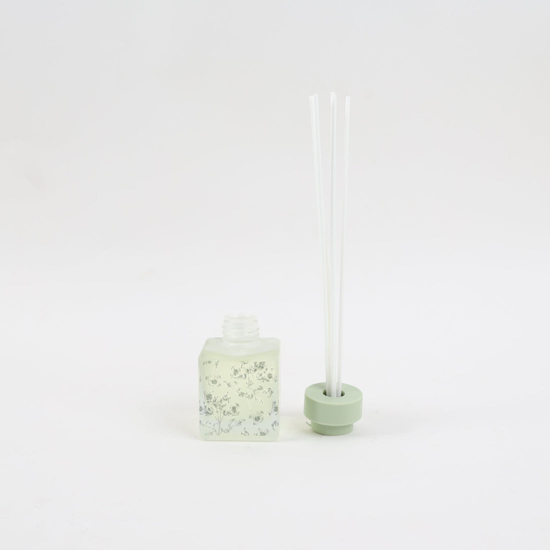 Reed diffuser bottle with pale green cap and three clear fragrance reeds