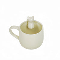 White ceramic mug with cat topper figurine and open cup interior.