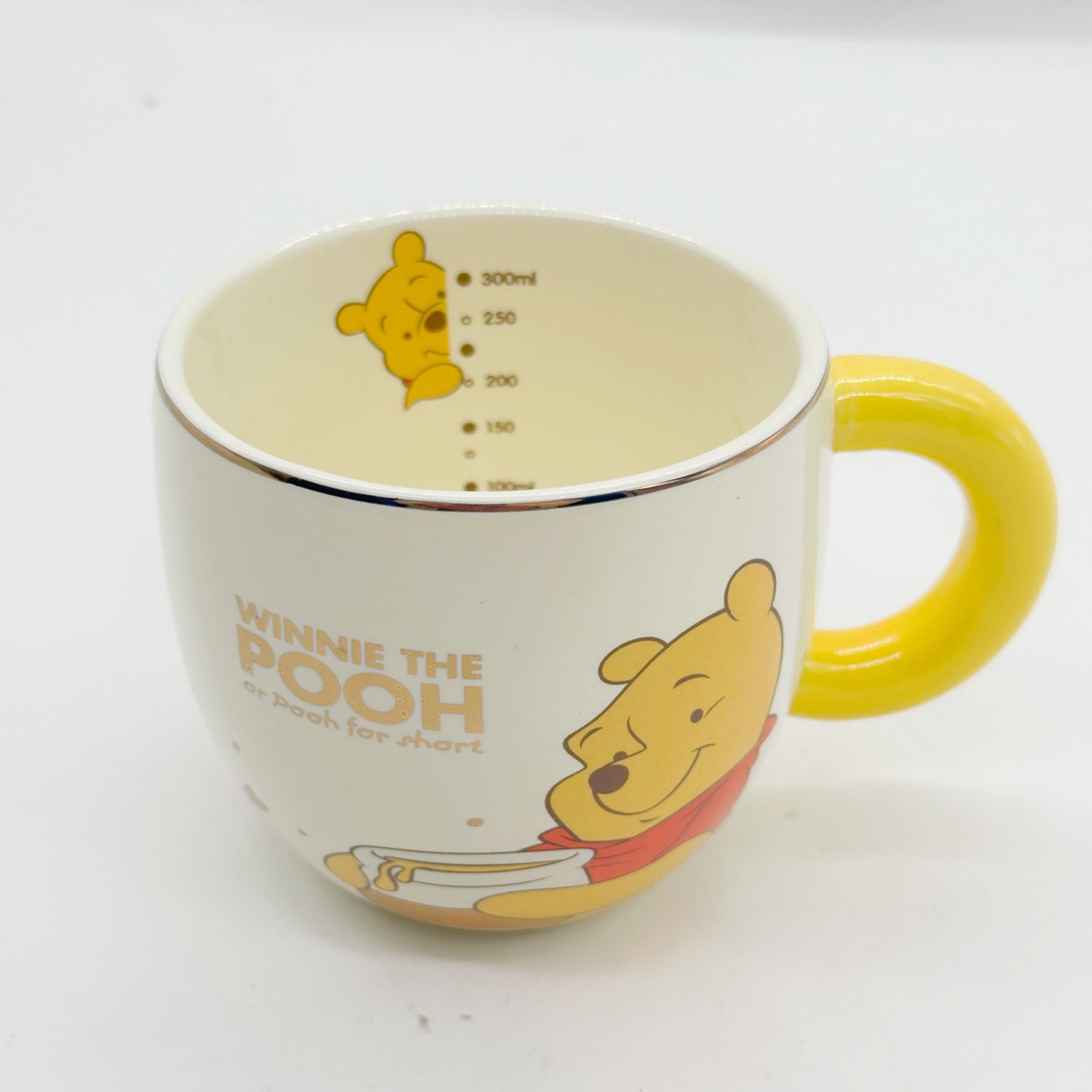 Cream Winnie the Pooh mug with yellow handle; cartoon print and interior measurement marks