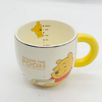Cream Winnie the Pooh mug with yellow handle; cartoon print and interior measurement marks