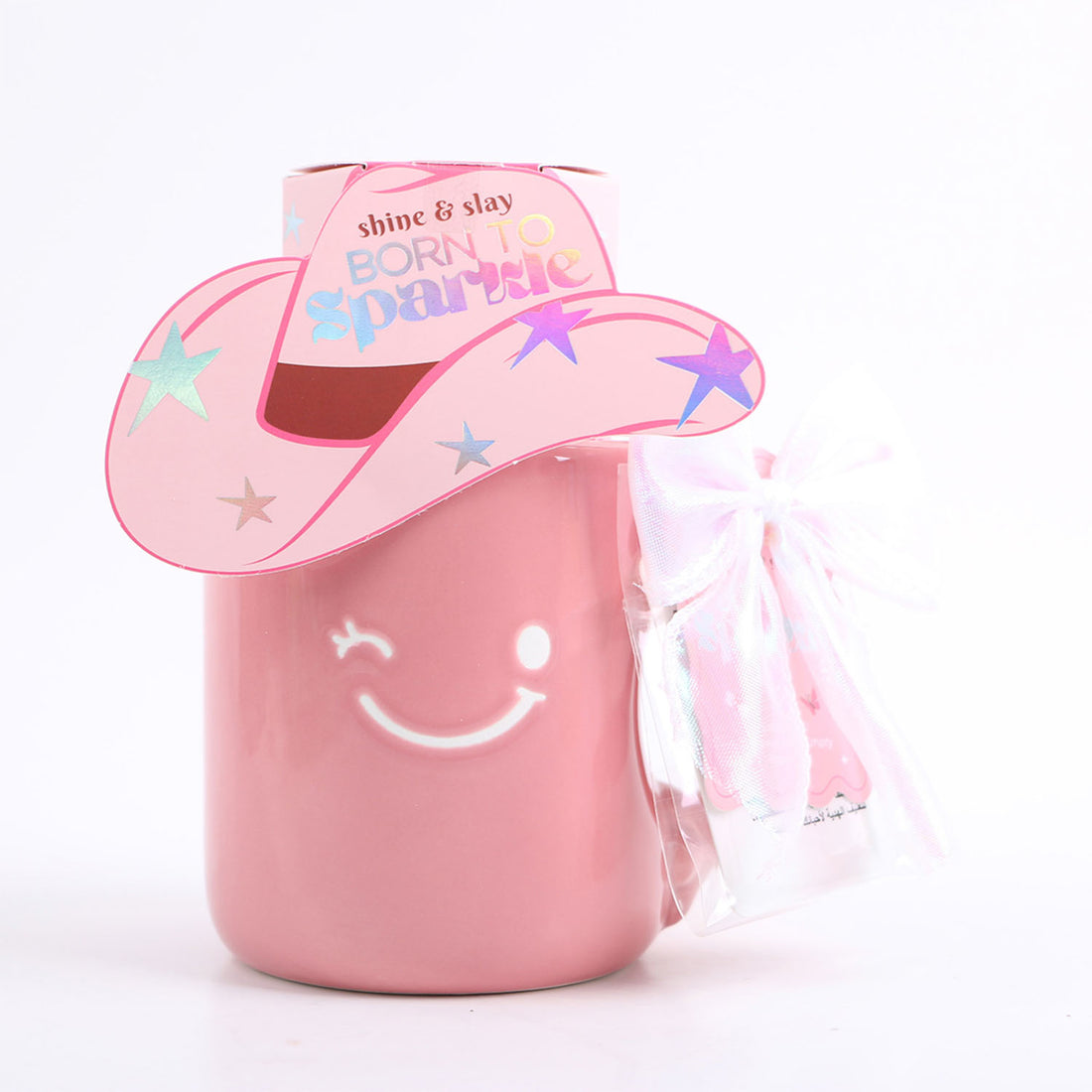Pink ceramic mug with unicorn-hat lid and white ribbon bow, paper box at back