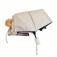 Folding umbrella, beige canopy with cream handle and tan fabric tie bundle.