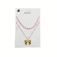 Gold necklace with pink bead accents and bow charm pendant