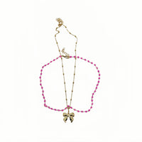 Gold necklace with pink beaded loop and bow charm pendant