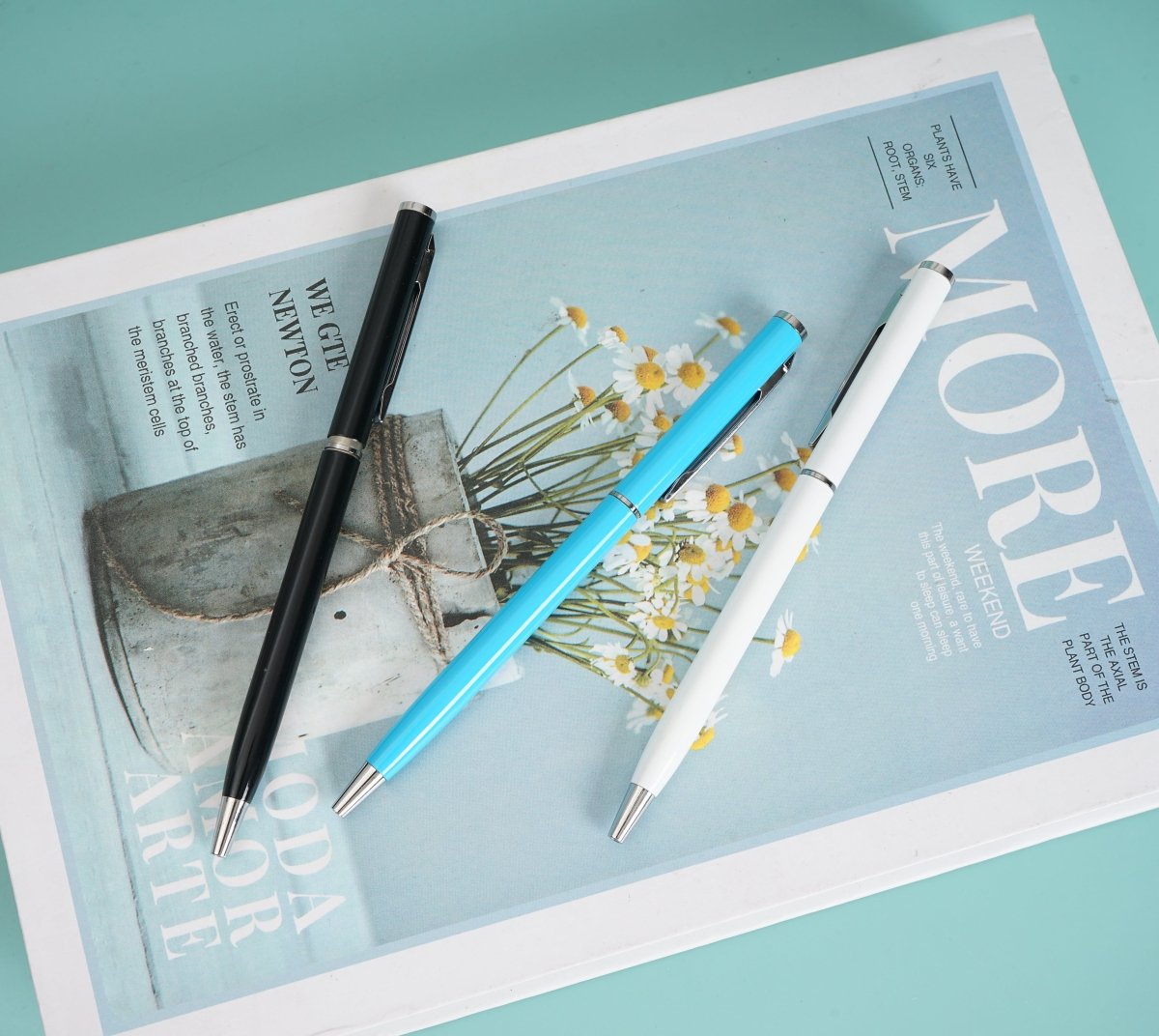 Three ballpoint pens (black, blue, white) on a paper cover