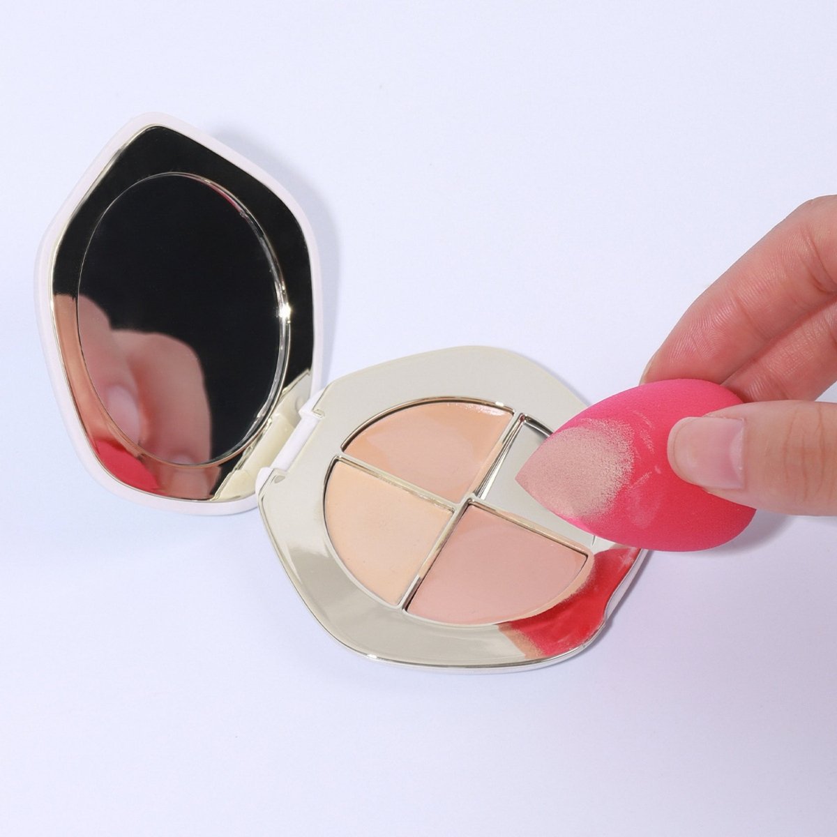 Makeup sponge puffs in a compact case, one sponge held between fingers