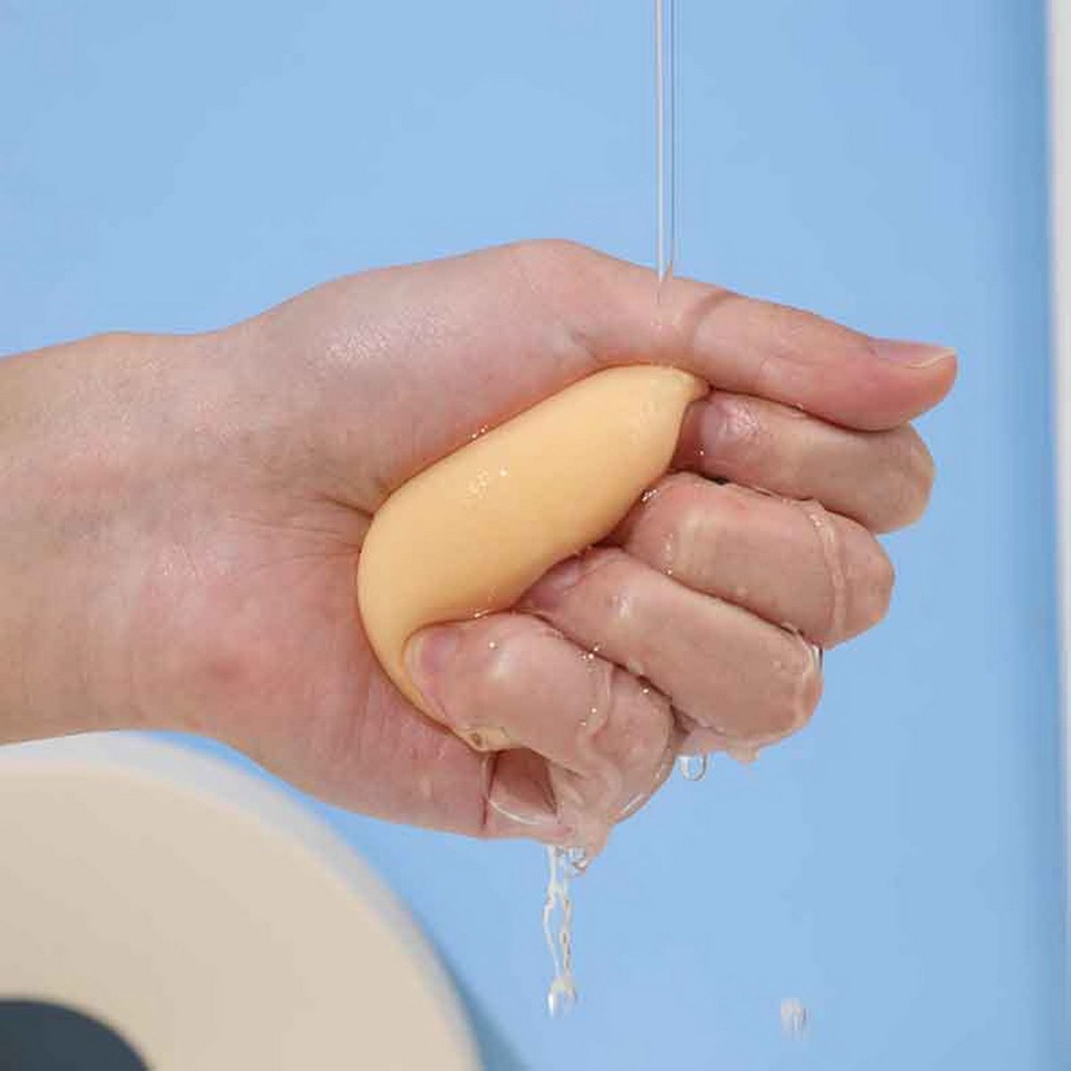 Teardrop makeup sponge held under running water, yellow with droplets