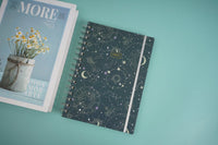 Celestial notebook with dark cosmic cover, spiral binding, and silver side stripe.