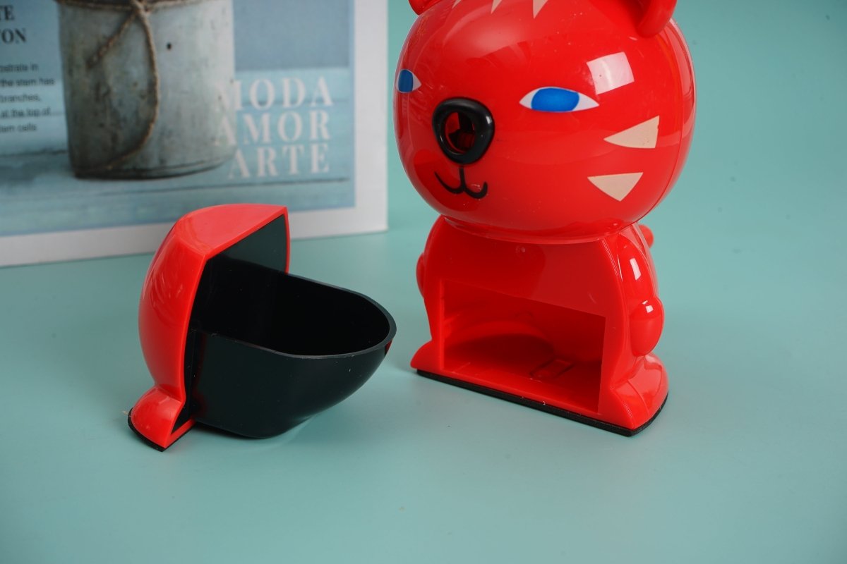 Red bear-shaped hand pencil sharpener with open shavings tray and blue-eyed face