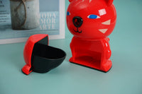 Red bear-shaped hand pencil sharpener with open shavings tray and blue-eyed face