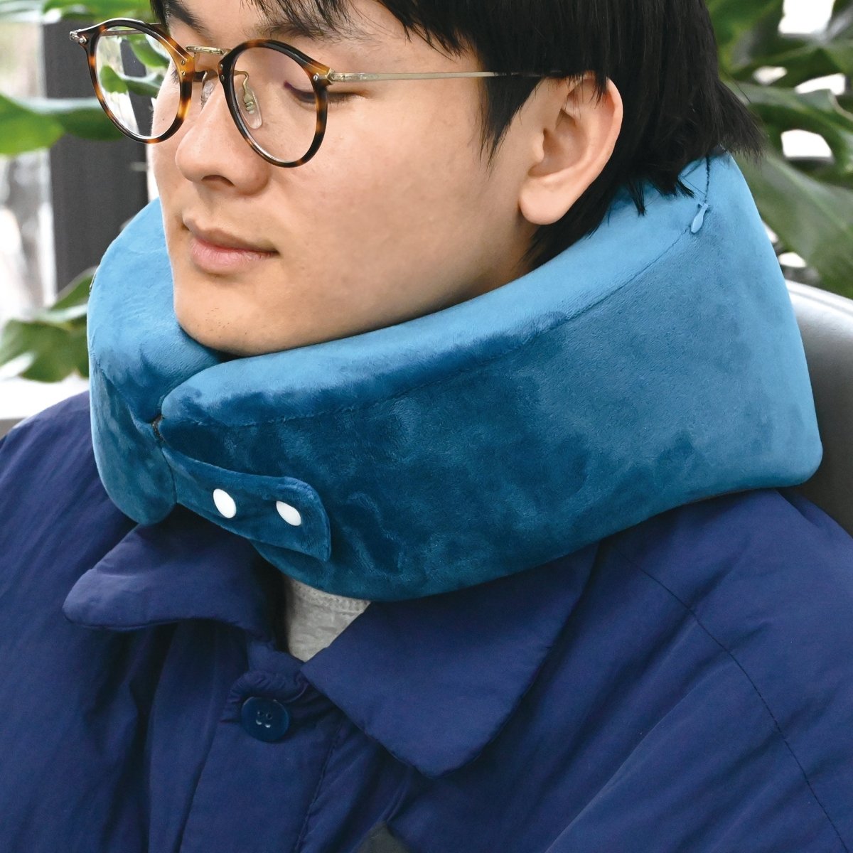 Blue travel neck pillow worn around the neck, with a two-button strap under the chin