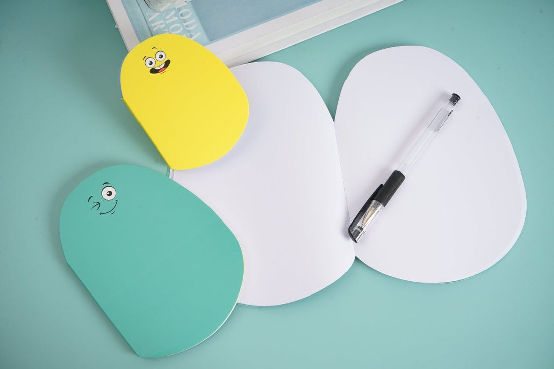 Worm-shaped notebook set with three pastel covers and cute bug faces; pen on white cover