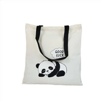 White canvas tote bag with panda and 'GOOD LUCK' bubble, black side straps, buttoned top
