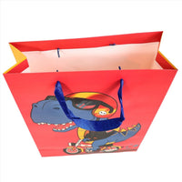 Dinosaur gift bag with cartoon blue dino riding a scooter, open top and red body