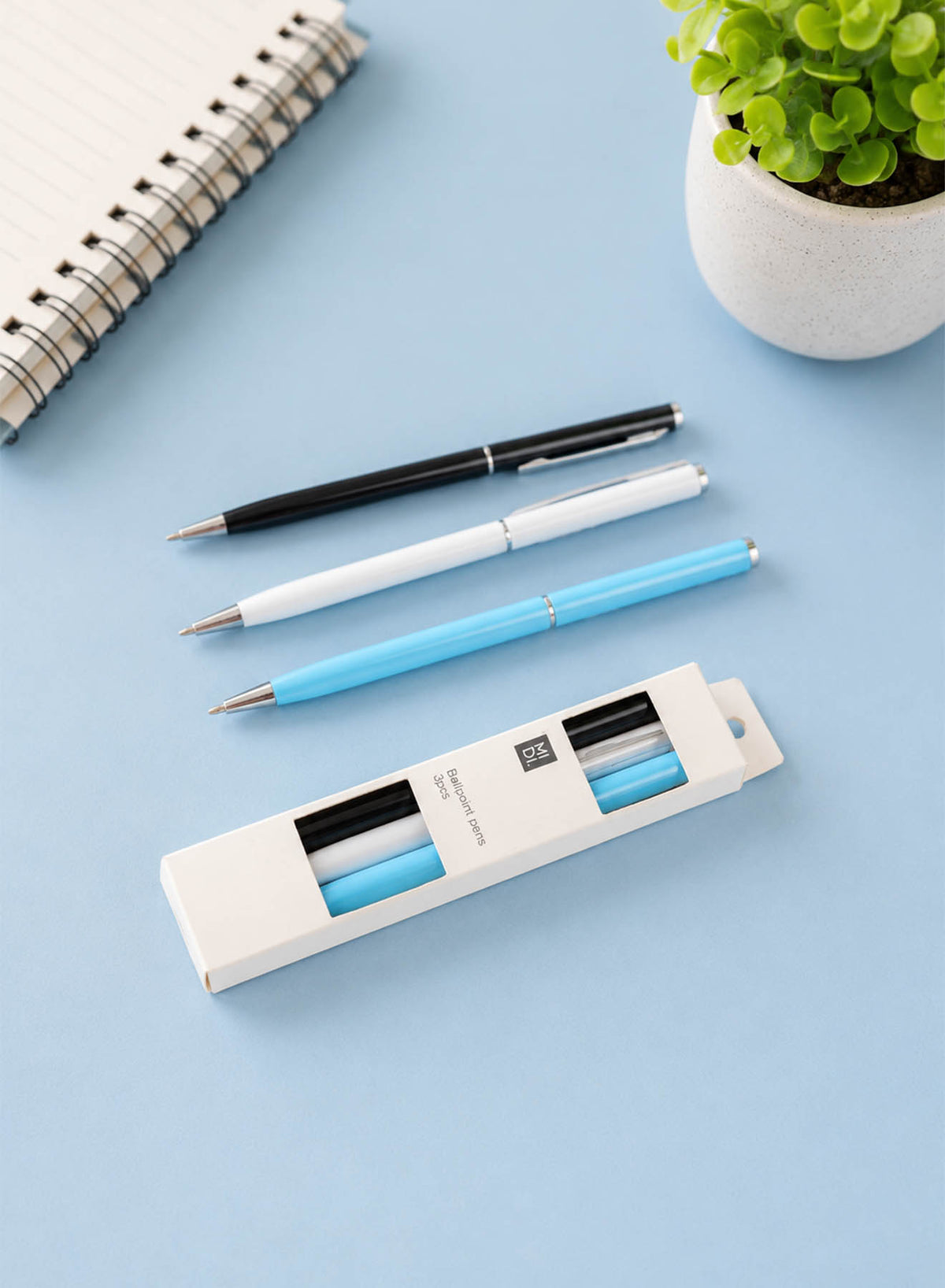 Three ballpoint pens in black, white, and light blue laid out with pen box