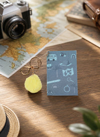 Blue mini notebook with yellow pom pom keychain and travel icon cover