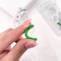 Eyelash curler with green grip held by fingers, white clamp arch.