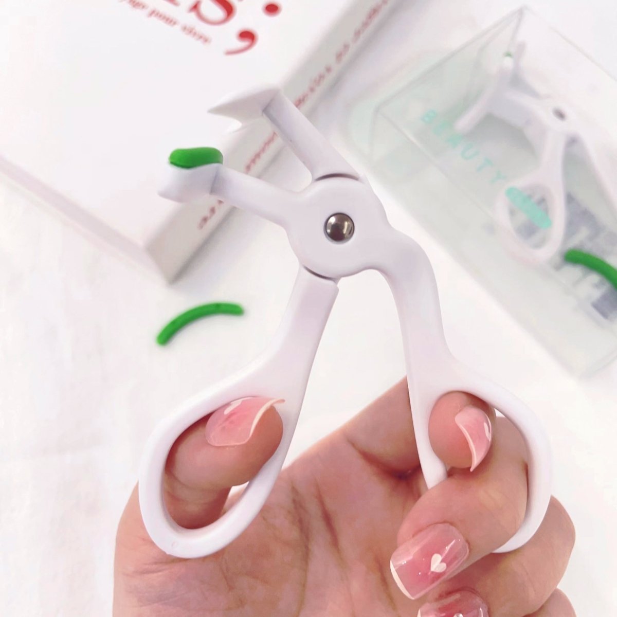 Eyelash curler used on lashes, white frame with green handle in hand.
