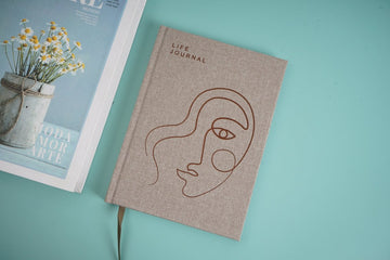 Cloth bound hardback notebook, taupe cover with line-art face and journal text