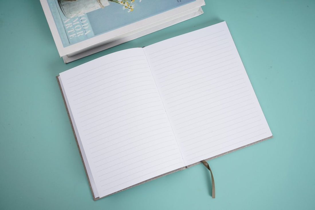Cloth bound hardback notebook opened, blank white lined pages with stitched spine
