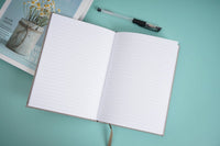 Cloth bound hardback notebook open flat, two white lined pages and cloth spine tie