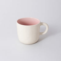 Ceramic cup with cream exterior and pink interior, rounded handle and smooth lip