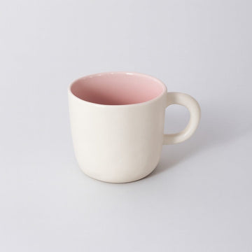 Ceramic cup with cream exterior and pink interior, rounded handle and smooth lip