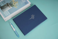 Hardback daily planner notebook, dark blue cover with embossed design and matching pen