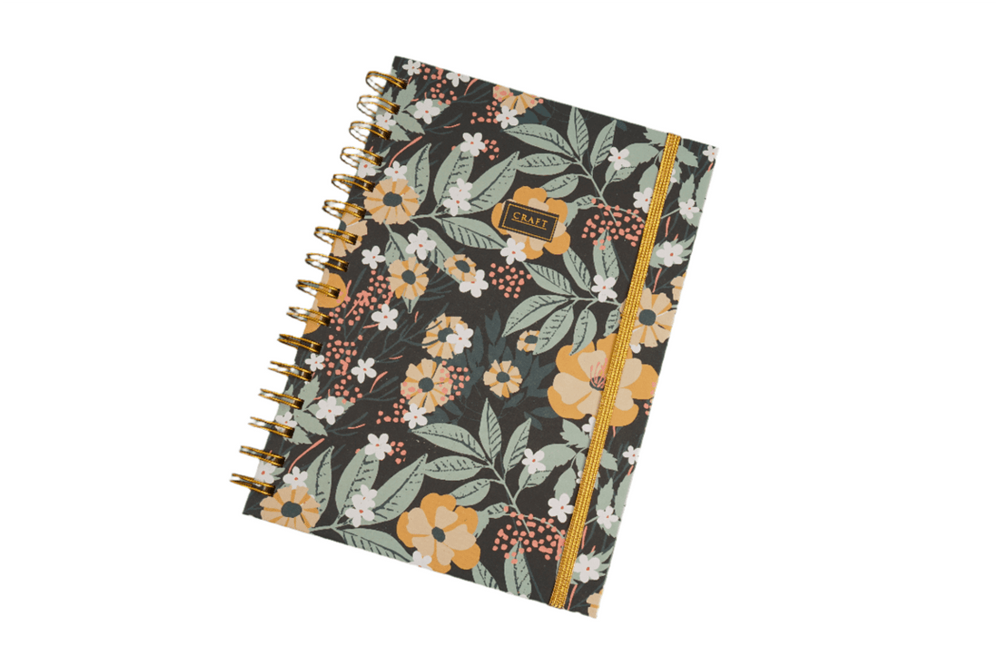 Hardcover spiral notebook with dark floral cover and gold ring binding, front view.