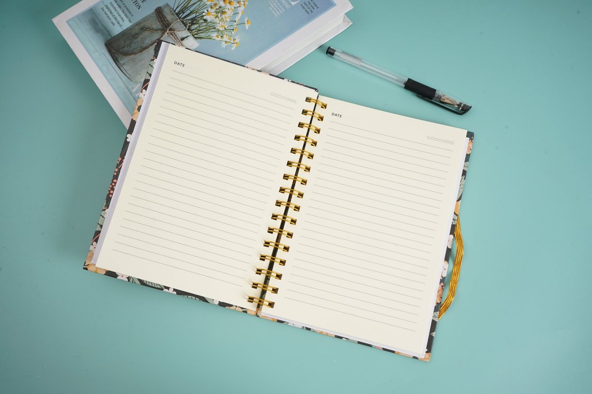 Open hardcover spiral notebook with lined pages and gold rings, flat lay view.