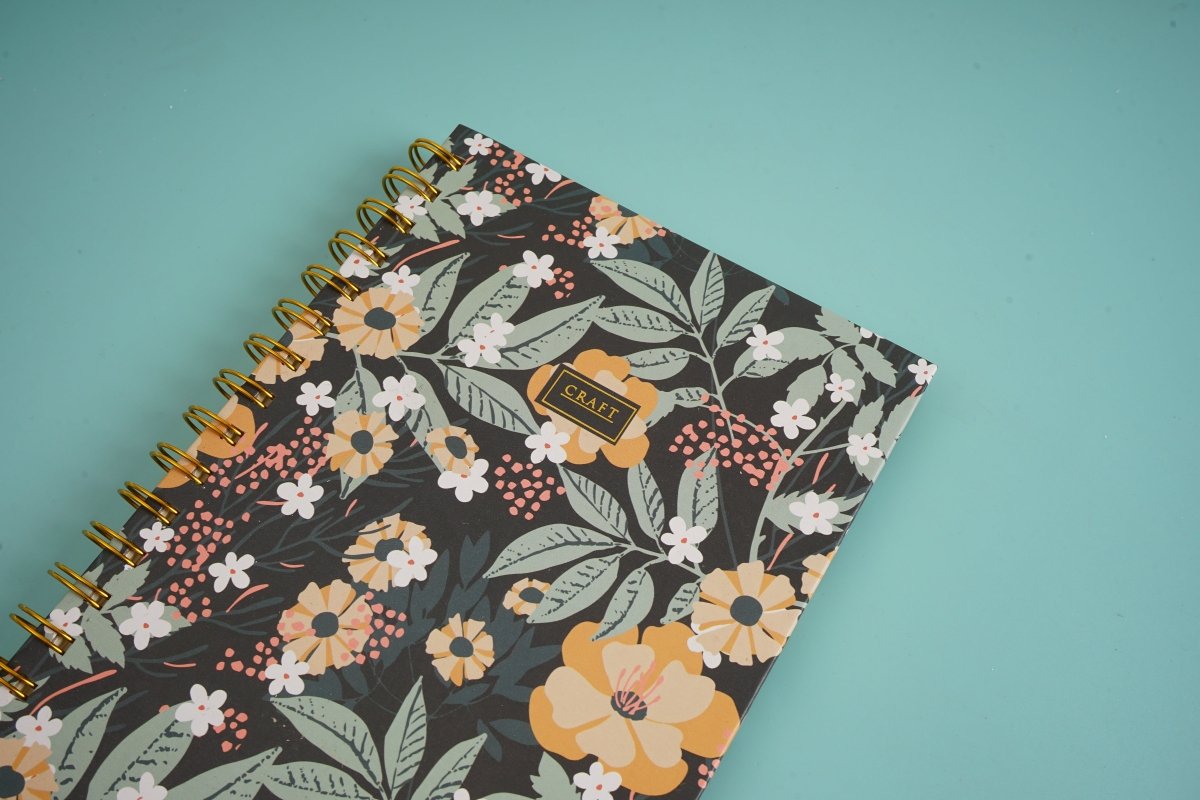 Hardcover spiral notebook cover close-up with dark floral pattern and gold rings.