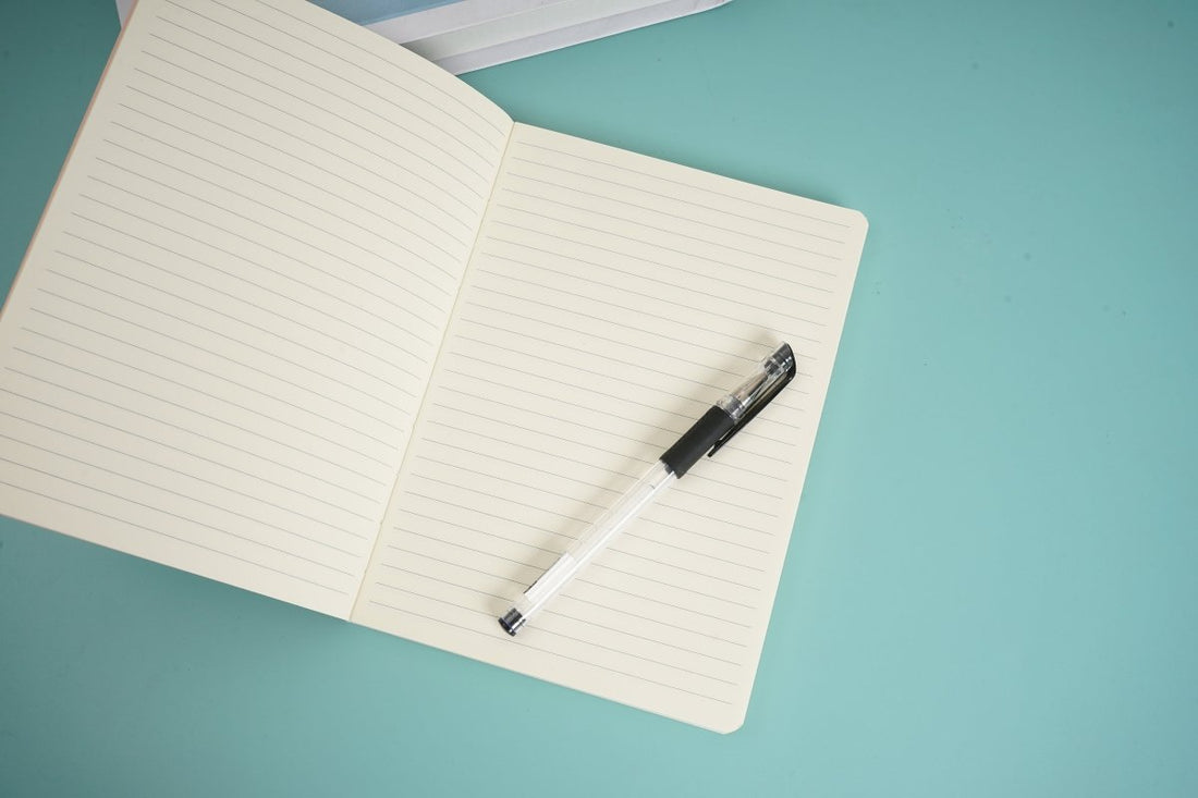 A5 lined notebook open with pen resting on blank ruled pages