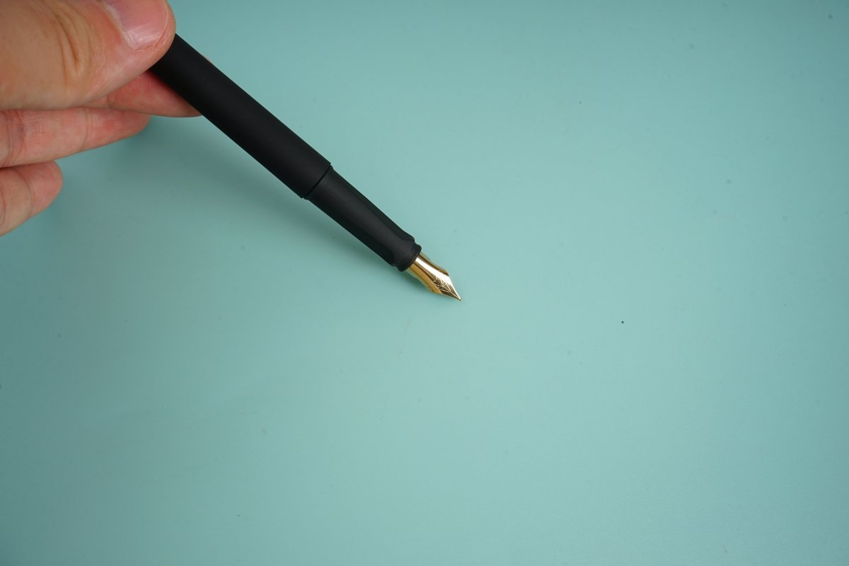 Black fountain pen with gold nib held by a hand