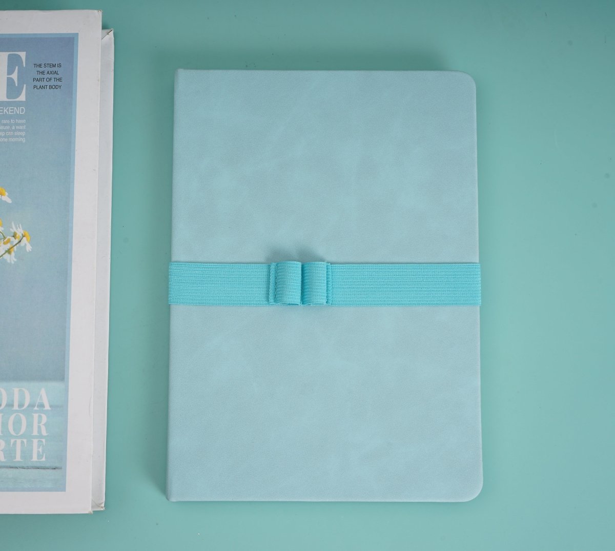 A5 PU cover notebook in light green with teal elastic band across front, closed.