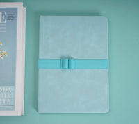 A5 PU cover notebook in light green with teal elastic band across front, closed.