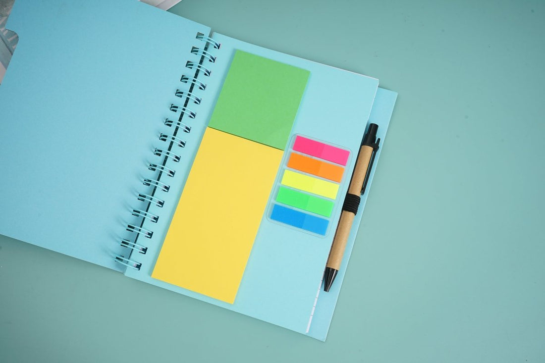 Spiral notebook with sticky notes and pen, open with colorful tabs and yellow sticky note