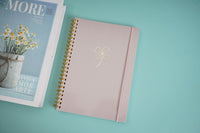 Pink elegant notebook with gold spiral binding and white bow on front cover