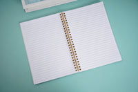 Open notebook with white lined pages and gold spiral rings, viewed from above