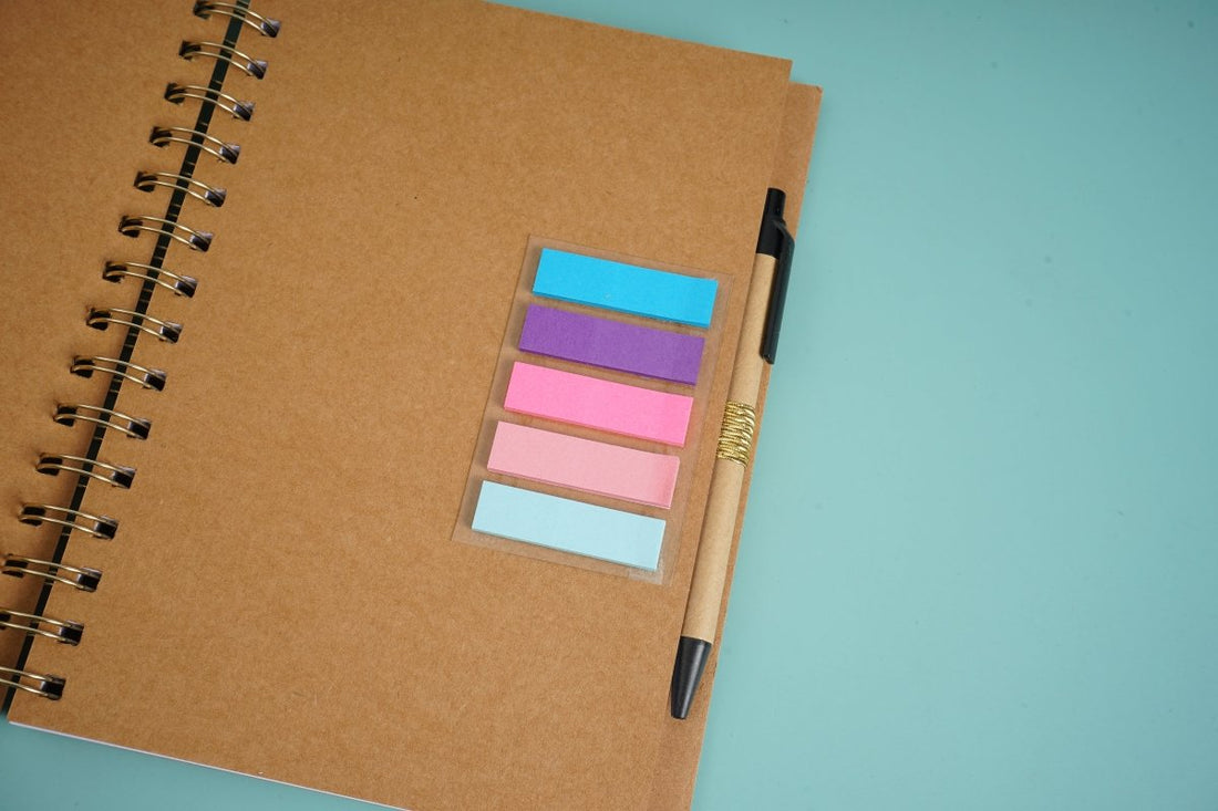 Kraft brown notebook with gold spiral coil, pen, and pastel sticky tabs