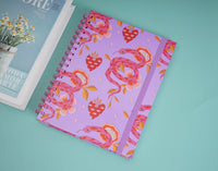 Purple notebook angled view, pink snake and floral pattern with spiral coil.